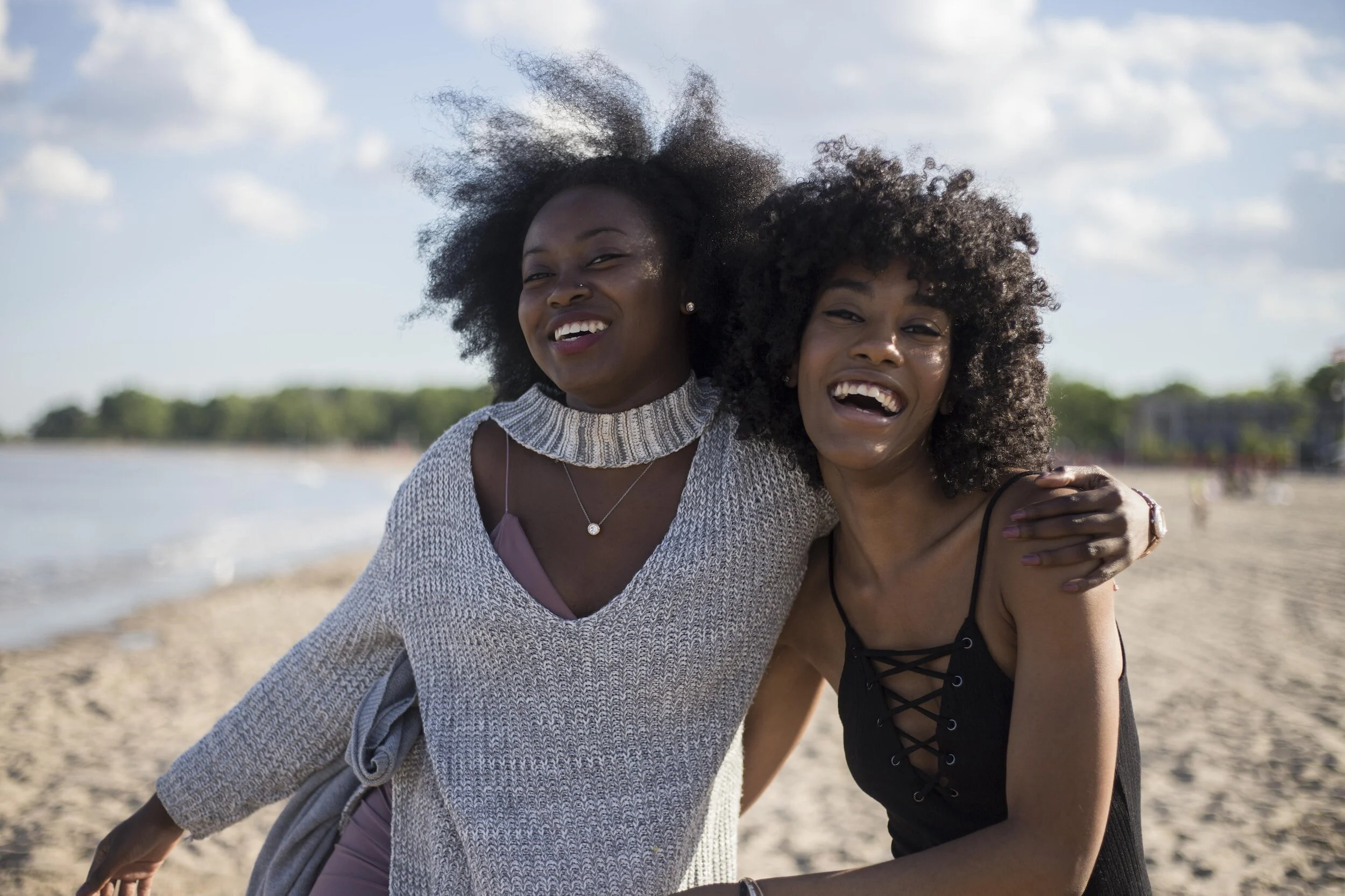 Two smiling Black women embracing on a sunny Toronto beach