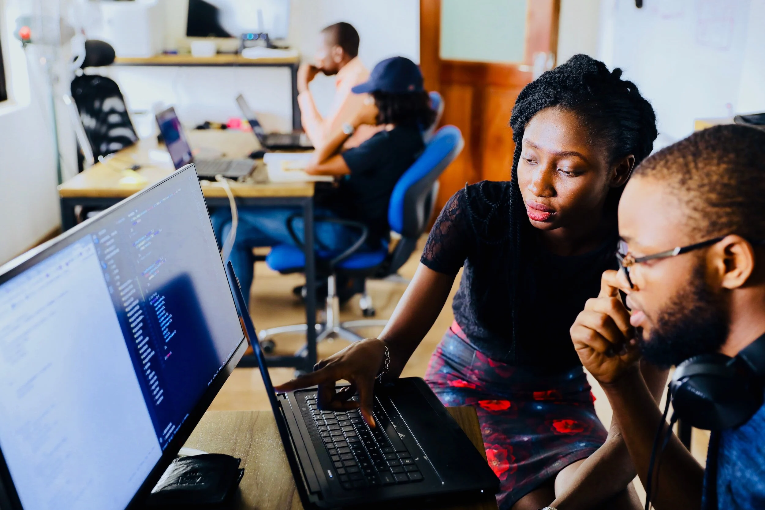 Two young Black professionals working together at a computer in a bright shared office