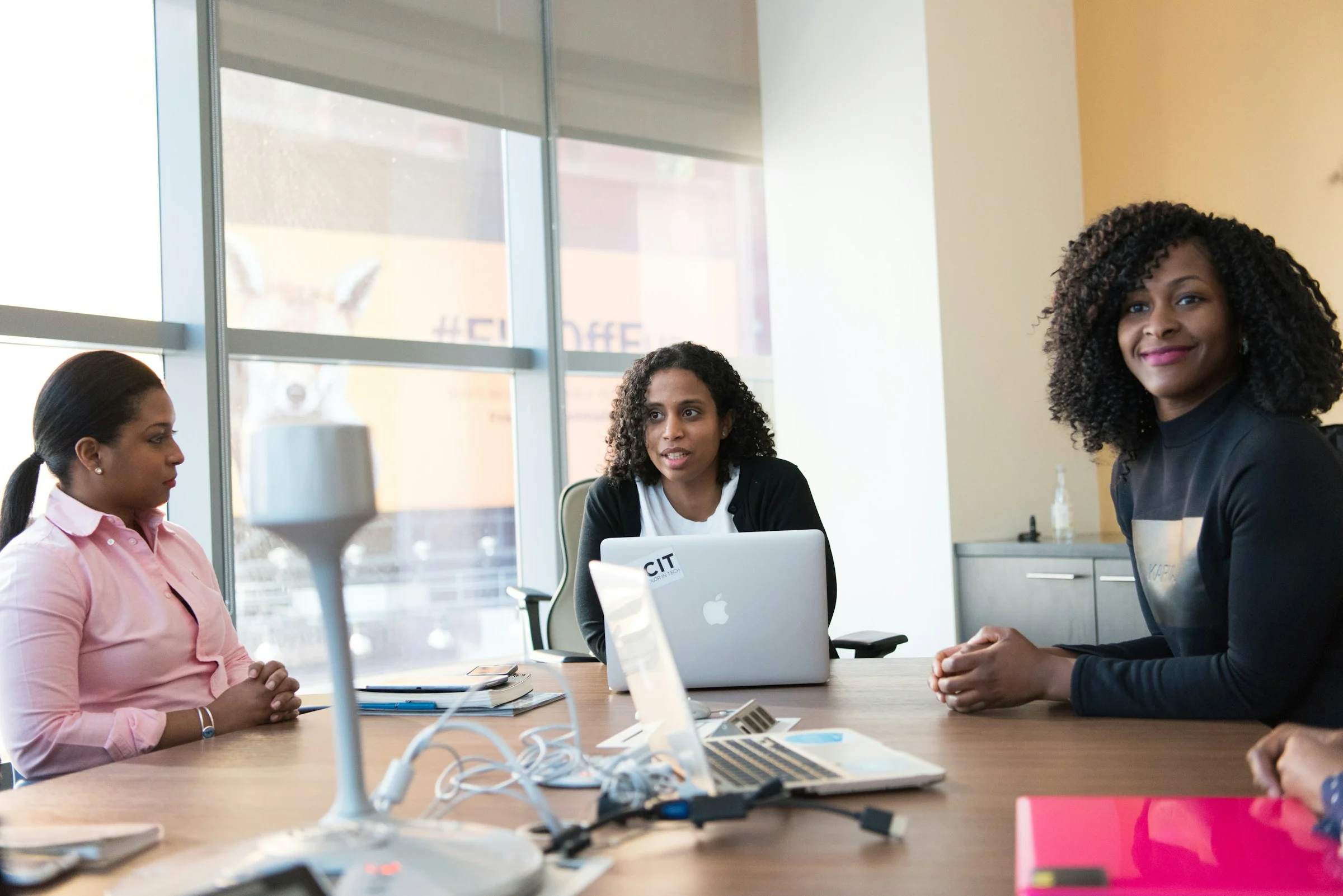 Three colleagues in conversation at a table with a laptop