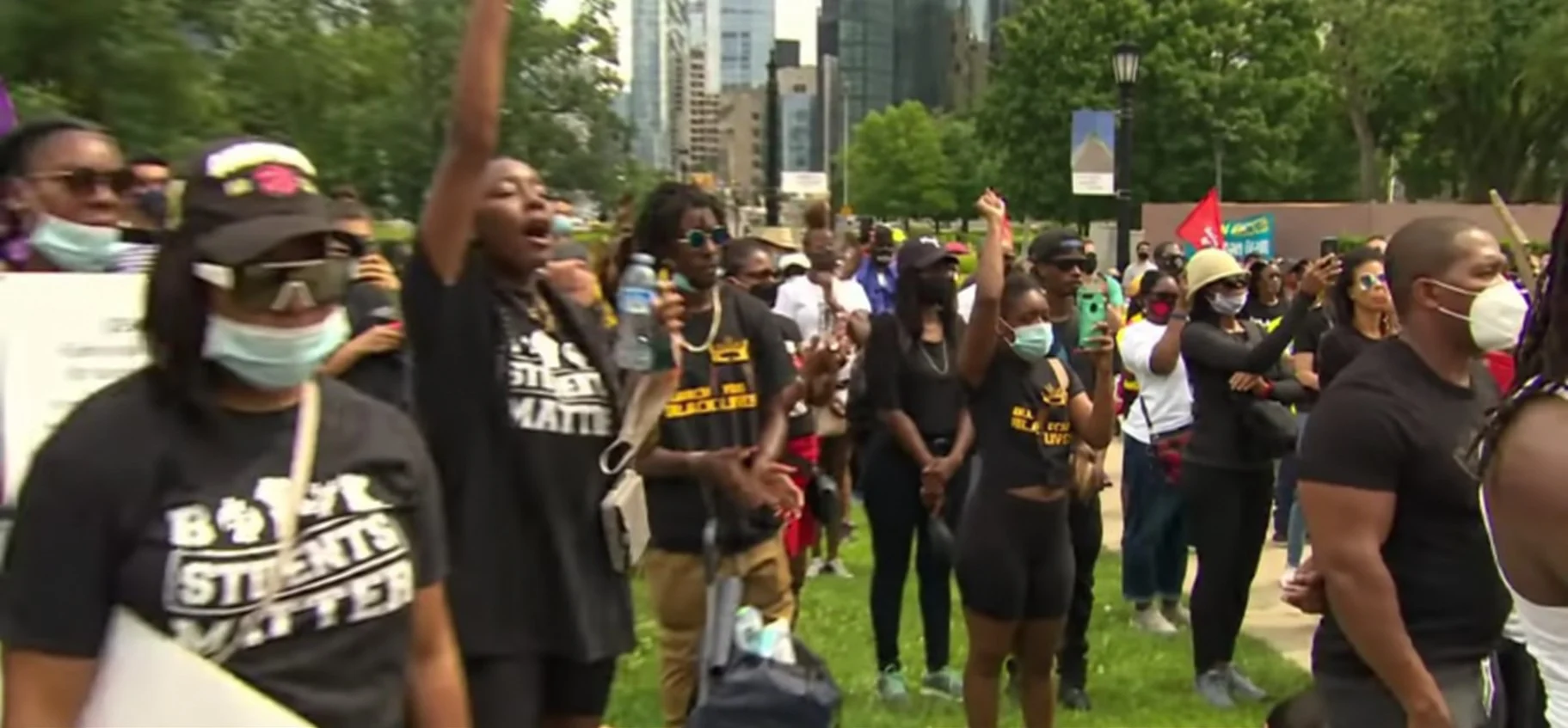 Demonstrators in Black Students Matter shirts raise their fists at an outdoor rally