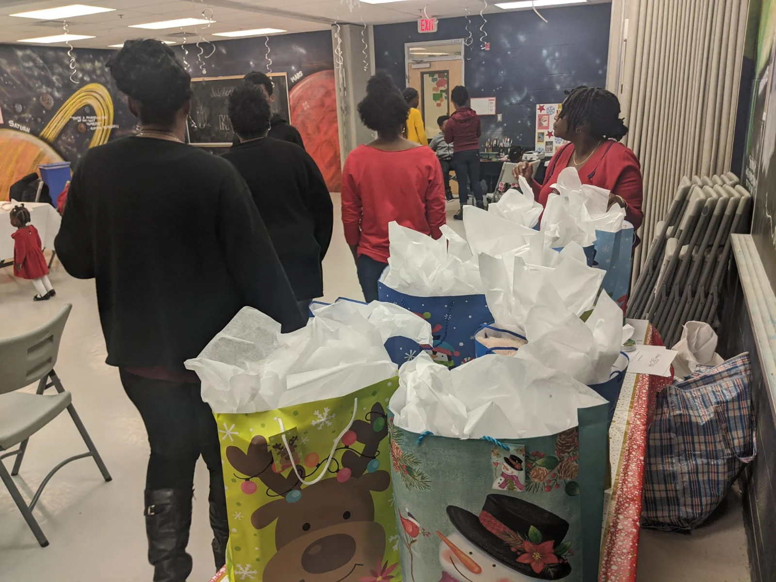 Women gather beside a table of wrapped holiday gift bags