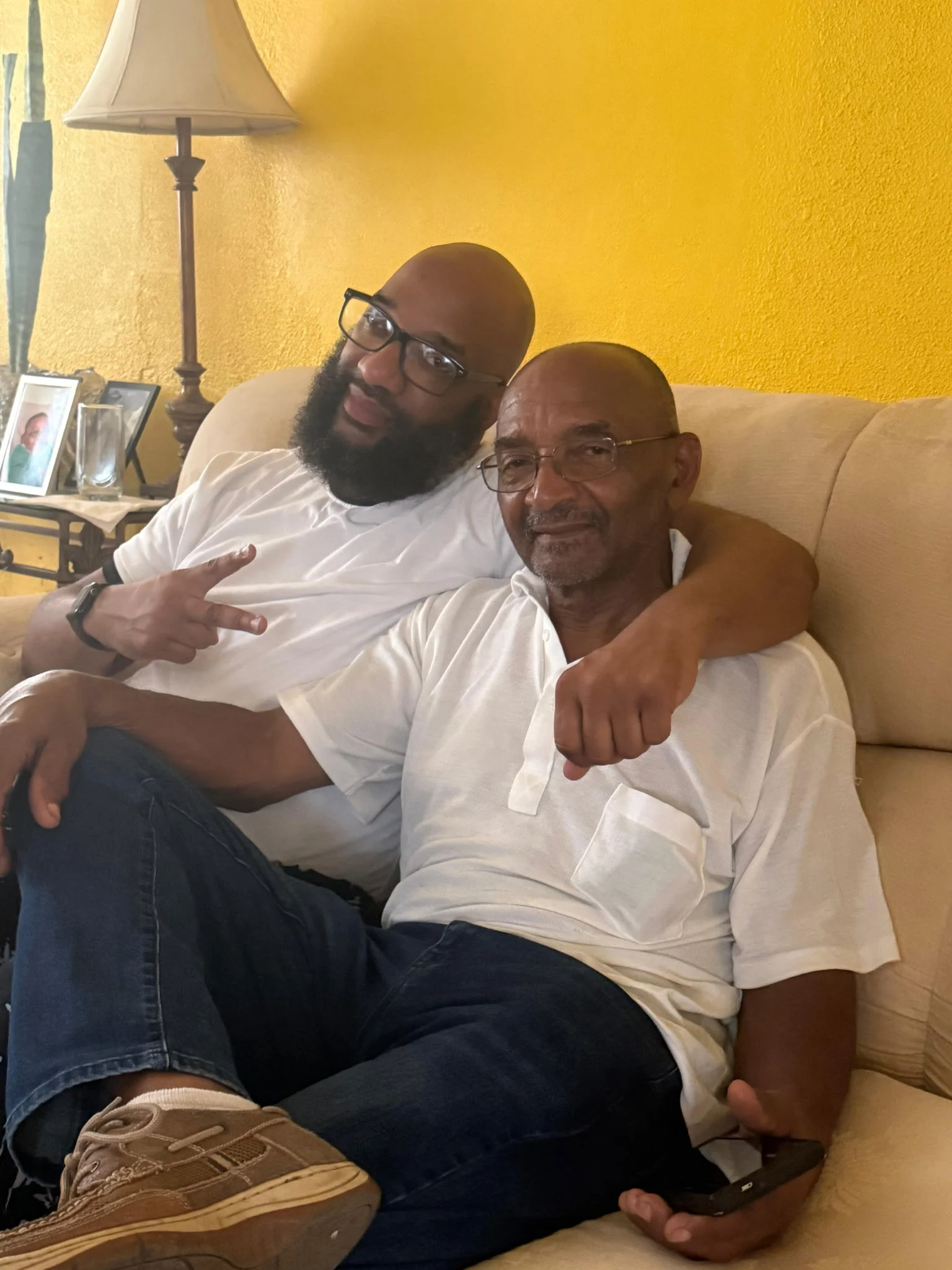 An older man and a younger man sit together on a couch, smiling